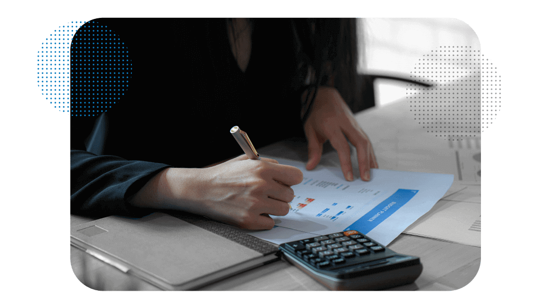 Pessoa do setor financeiro fazendo previsão orçamentária em papéis com gráficos e uma calculadora ao lado.